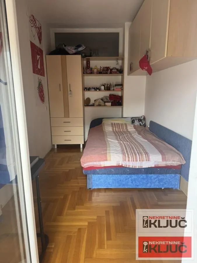 Manja spavaća soba sa krevetom, ormarom i drvenim podom.