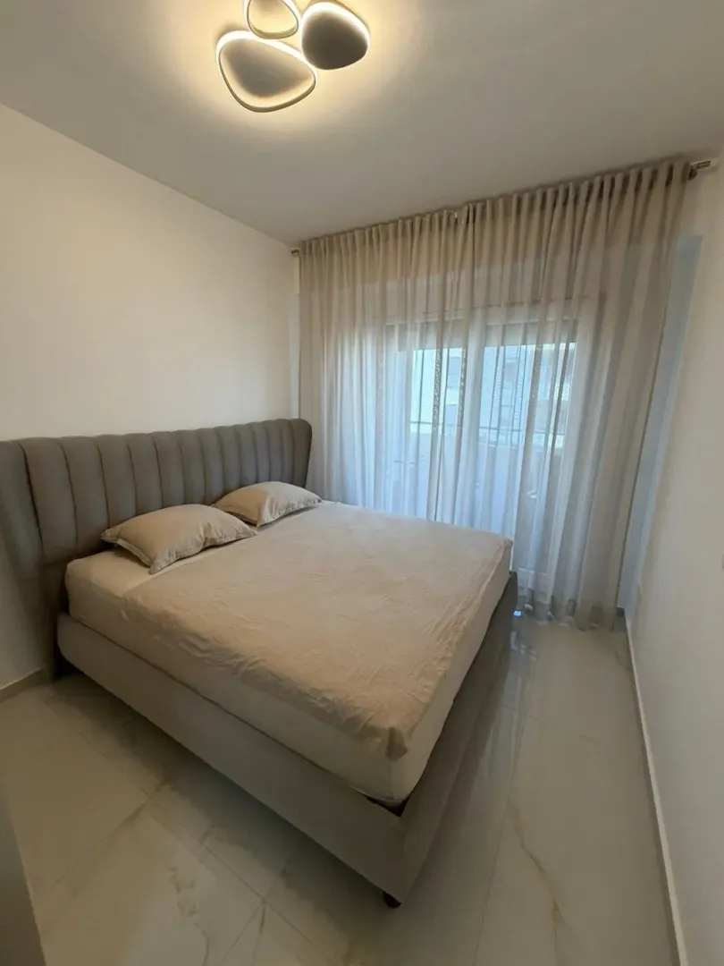 Uređena spavaća soba sa bračnim krevetom i prozorom sa zavjesama.