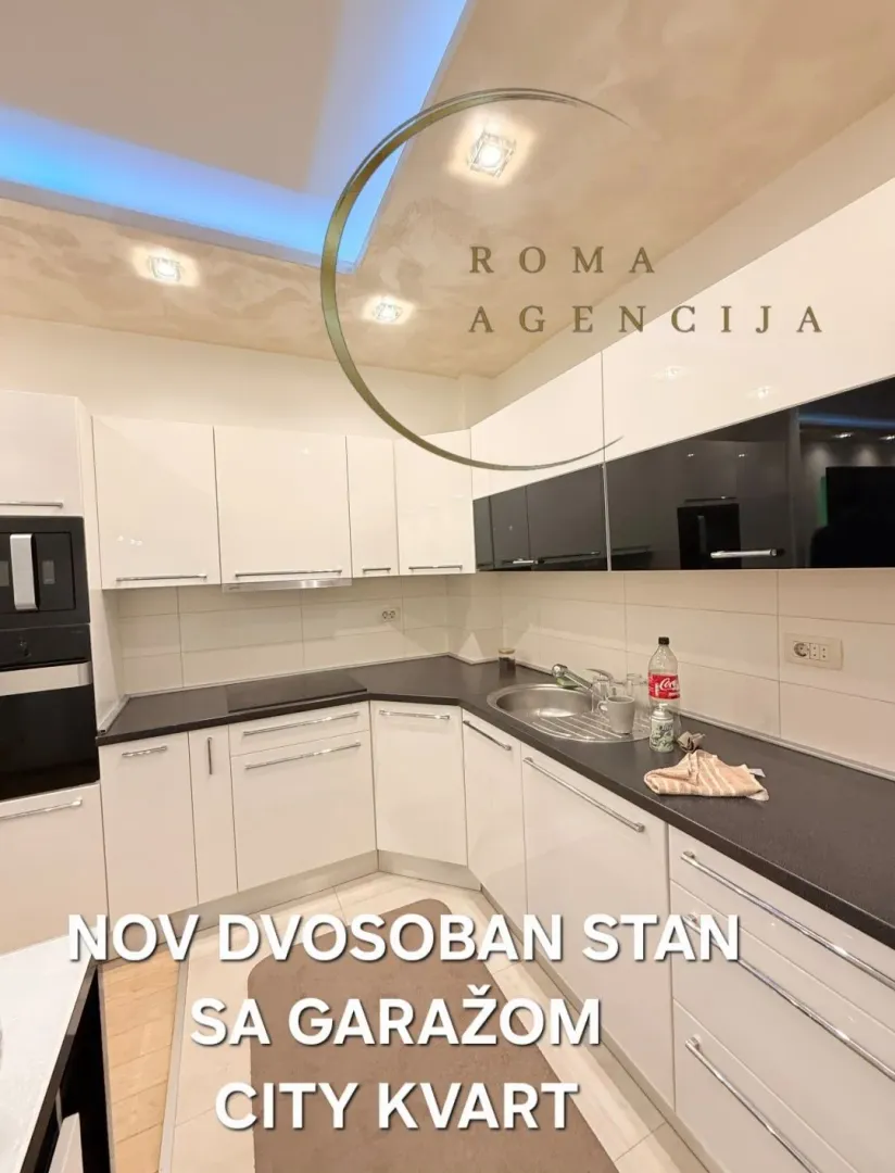 Moderna bijela kuhinja sa tamnim radnim površinama u stanu.