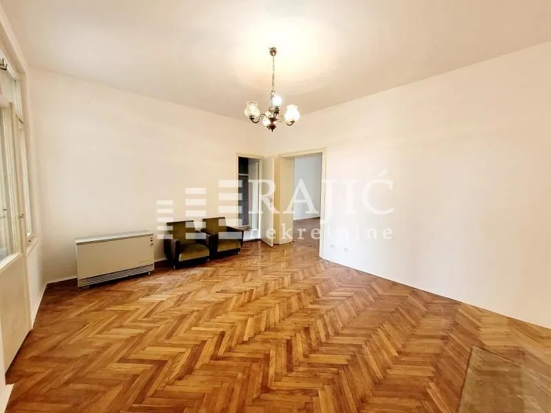 Spacious empty room with parquet flooring and a chandelier.