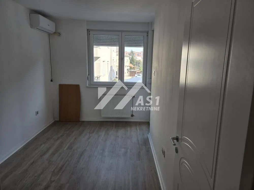 Empty room with a window, air conditioning unit, and laminate flooring.