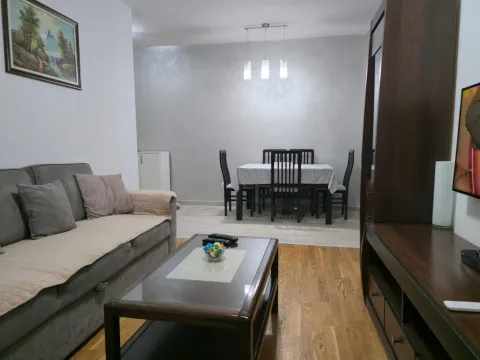 Living room with a sofa, coffee table, and dining area in the background. - image 3