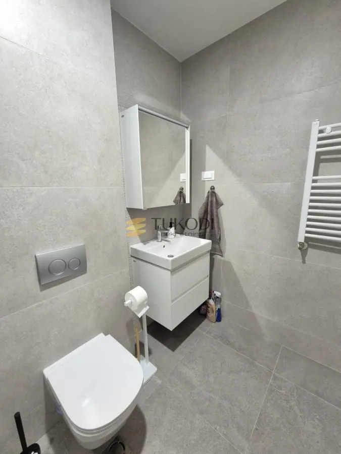 Modern bathroom tiled in grey with a wall-hung toilet and washbasin.