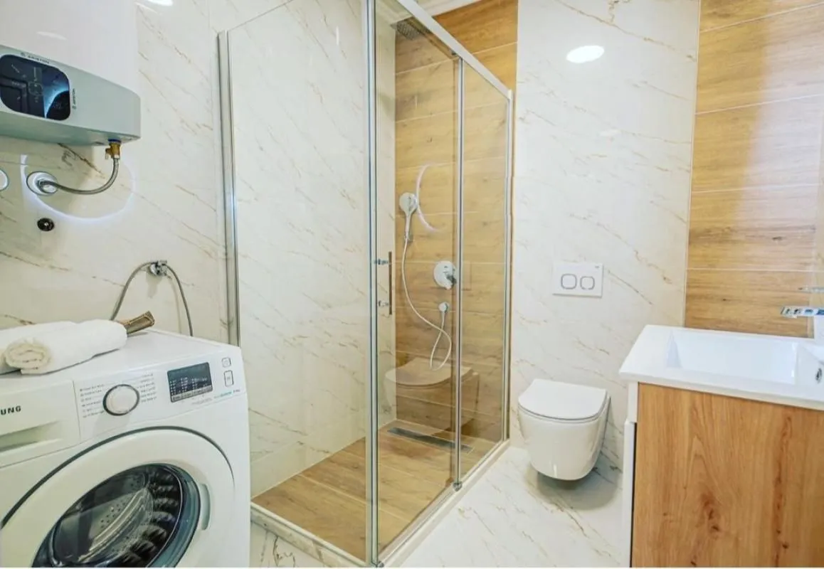 Modern bathroom equipped with a walk-in shower, toilet, vanity sink, and washing machine.