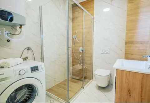 Modern bathroom equipped with a walk-in shower, toilet, vanity sink, and washing machine. - image 6