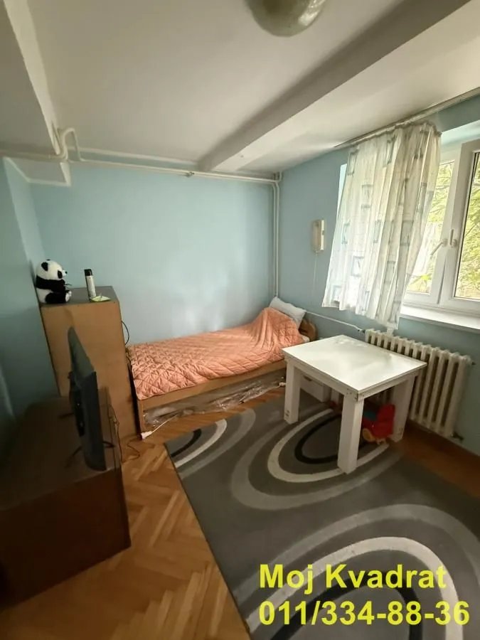 Manja spavaća soba sa krevetom, radnim stolom i televizorom.