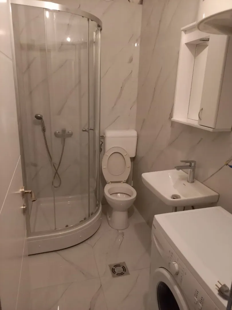 Bright bathroom featuring a shower cabin, sink, and washing machine.