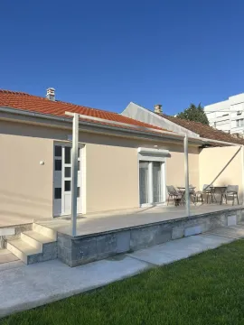 Exterior of a single-story house with a tiled terrace and a green lawn. - image 19