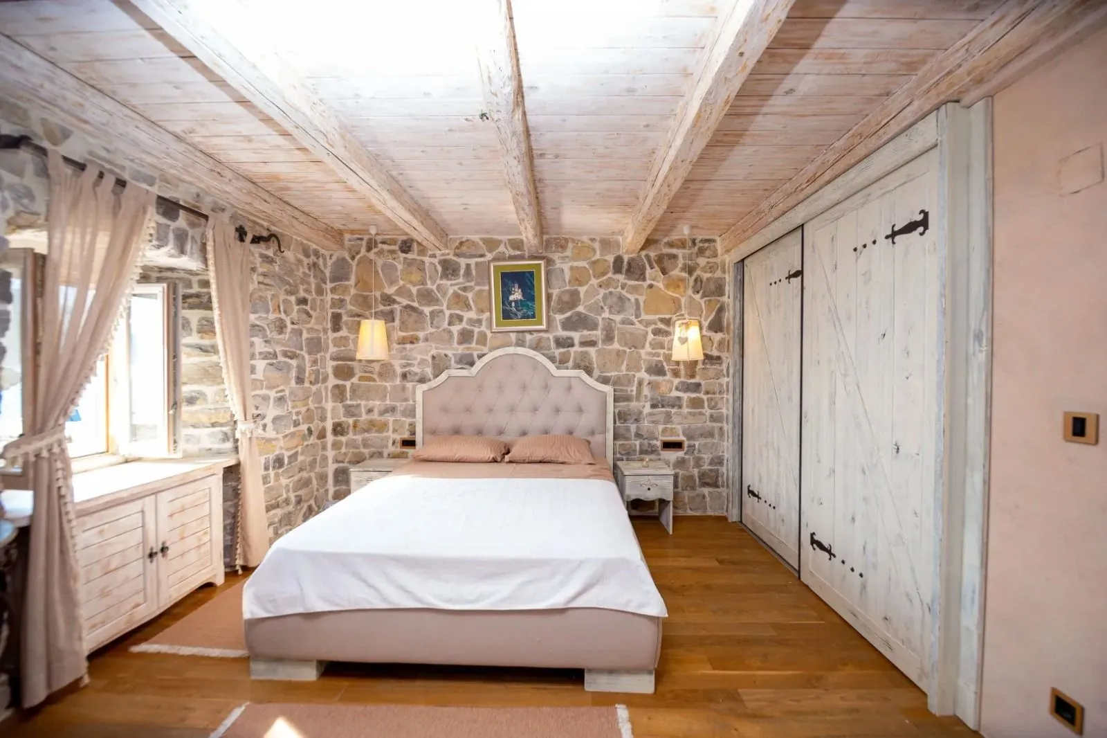 Bedroom with a double bed, stone wall, and wooden ceiling beams.