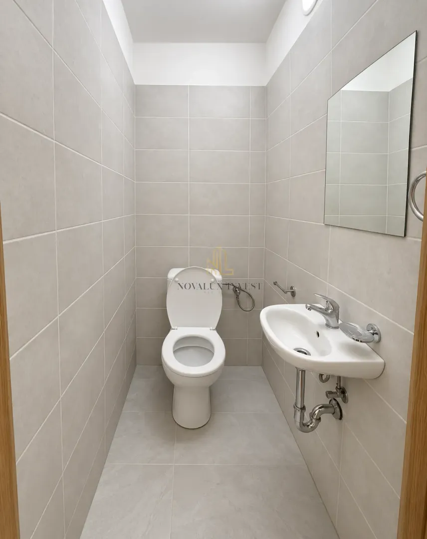 Savremeno opremljeno kupatilo sa WC šoljom, umivaonikom i ogledalom.