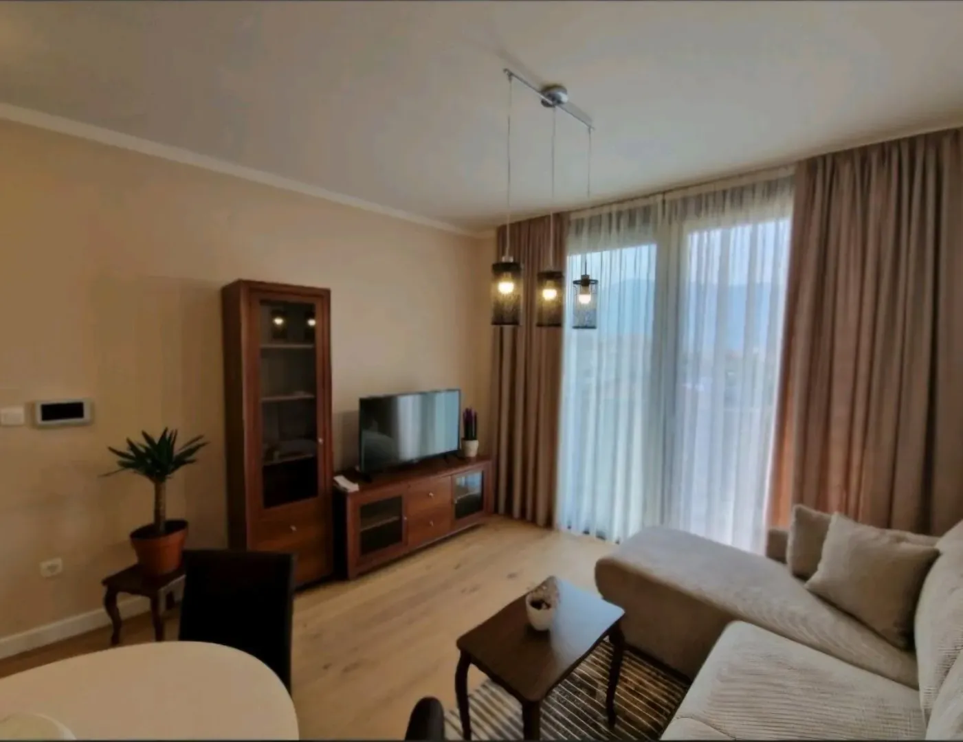 Udobna dnevna soba sa garniturom, TV-om i velikim balkonskim vratima.