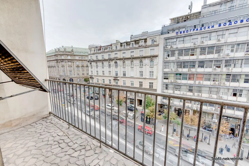 Balkon sa metalnom ogradom i pogledom na gradsku ulicu i okolne zgrade.