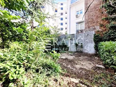 Overgrown courtyard with a wall and surrounding buildings in the background. - image 16
