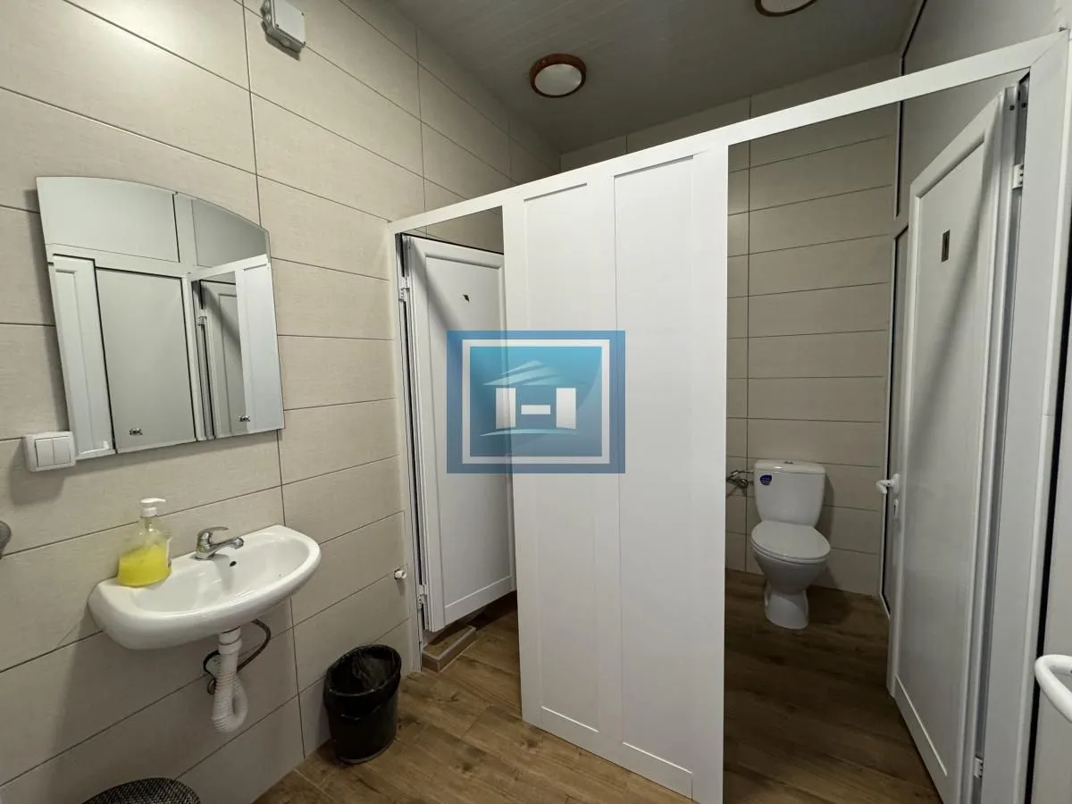 View of the bathroom with a sink, mirror, and separate toilet cubicles.