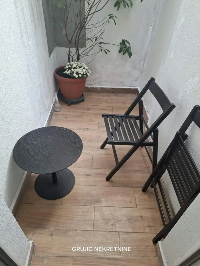 Small balcony with a wooden table, two chairs, and a potted plant.