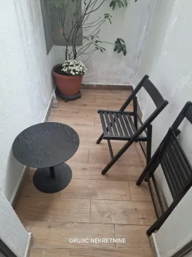 Small balcony with a wooden table, two chairs, and a potted plant. - image 8