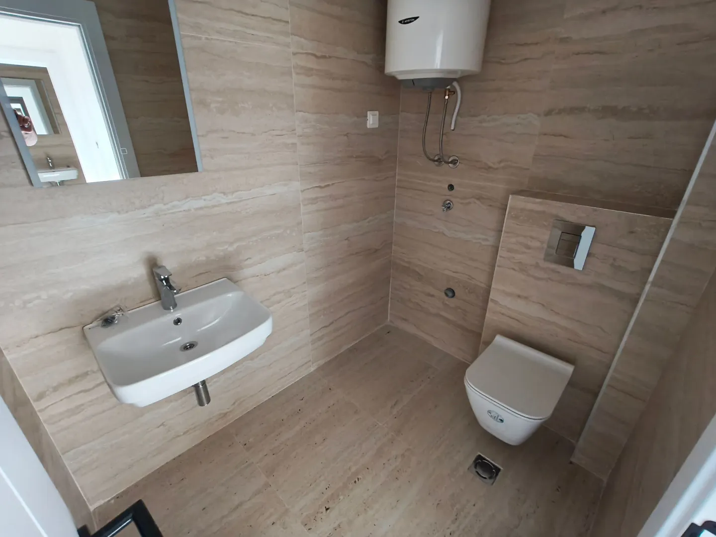 Kupatilo obloženo bež pločicama sa umivaonikom, wc šoljom i bojlerom.