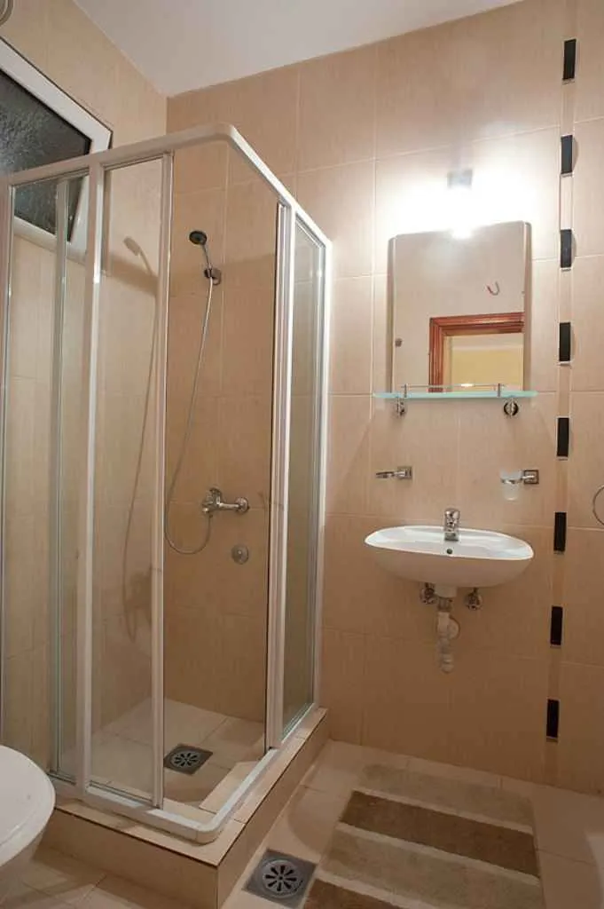 Jednostavno kupatilo sa tuš kabinom, lavaboom i ogledalom.