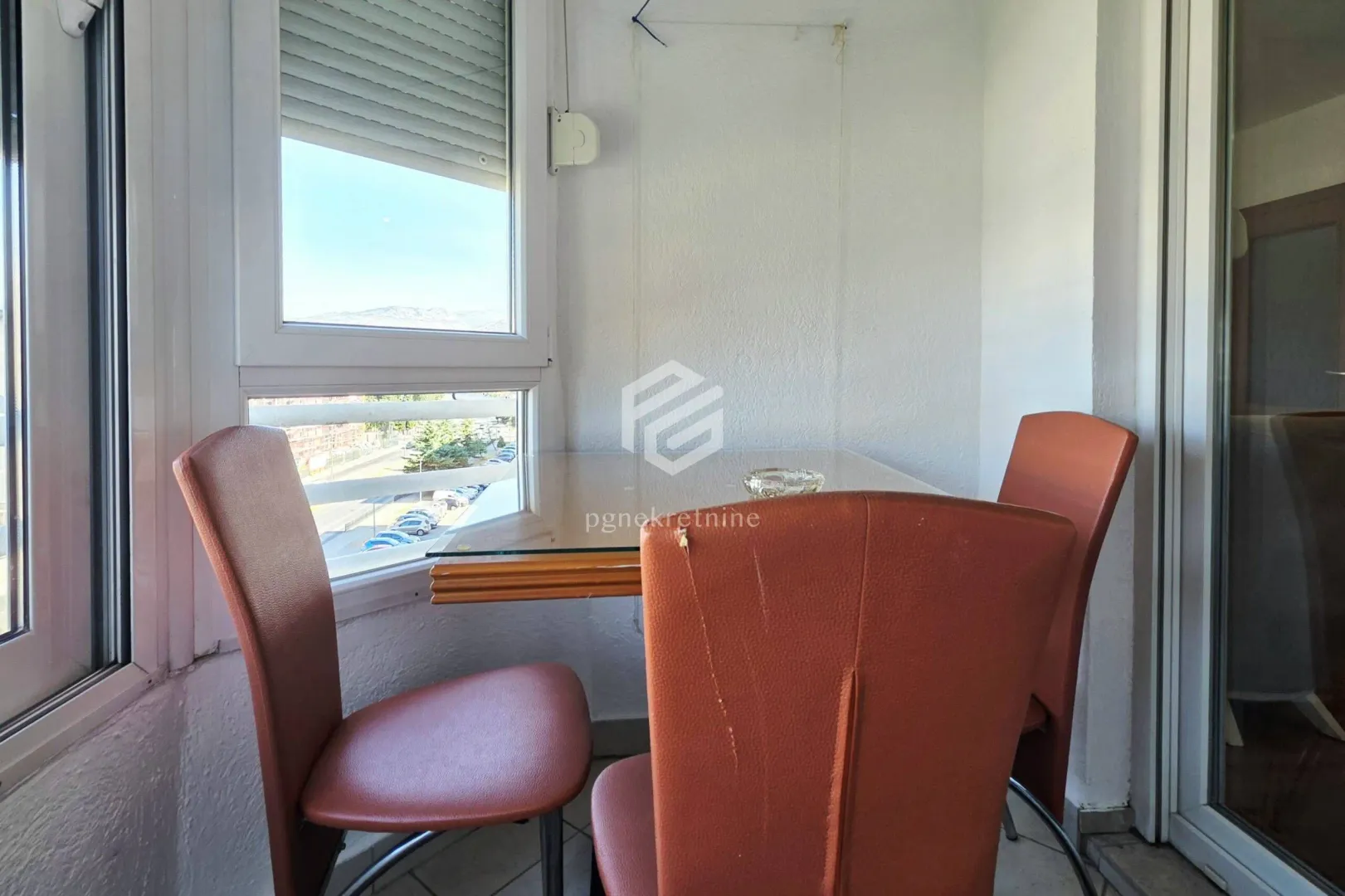 Enclosed balcony with a table and red chairs by the window.