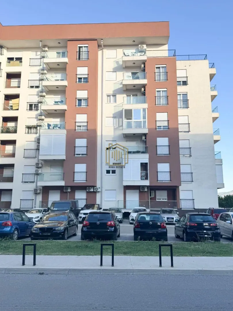 Fasada stambene zgrade sa terasama i parkingom ispred ulaza.