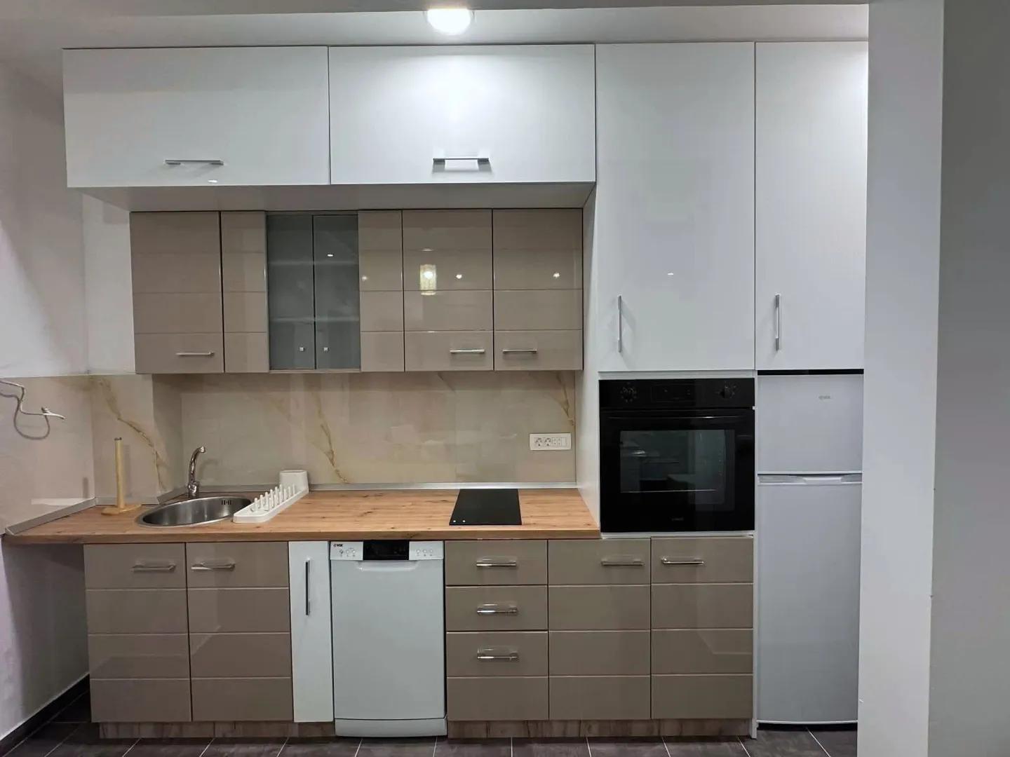 Modern kitchen with white and beige cabinets, built-in appliances, and a wooden countertop.