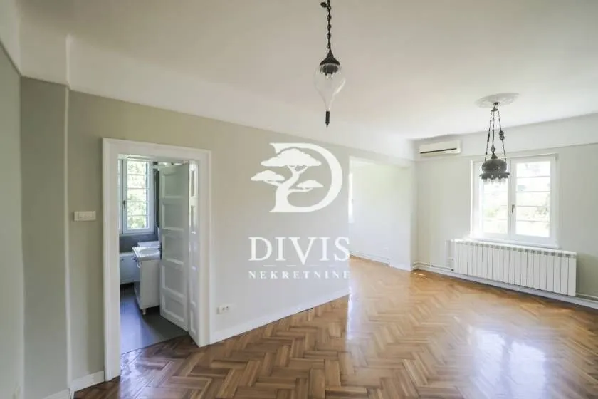 Spacious empty room with parquet flooring and a view into the bathroom.