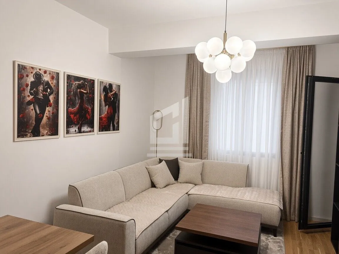 Dnevna soba sa ugaonom garniturom, stočićem i slikama na zidu.