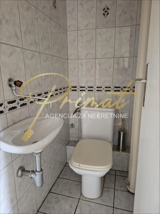 Manje kupatilo obloženo keramičkim pločicama sa umivaonikom i šoljom.