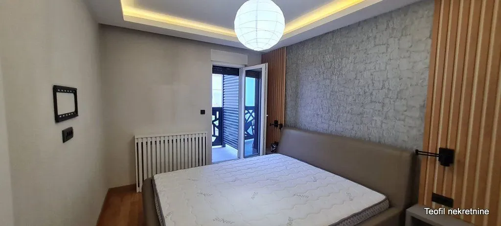 Nameštena spavaća soba sa bračnim krevetom i izlazom na terasu.