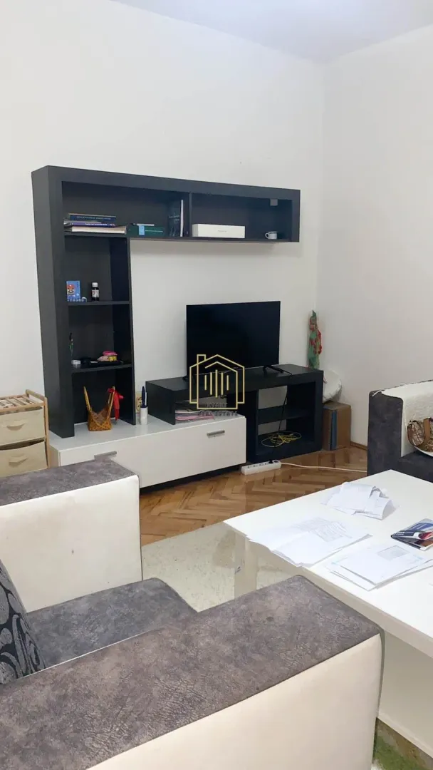Dnevna soba sa garniturom, TV komodom i policama.