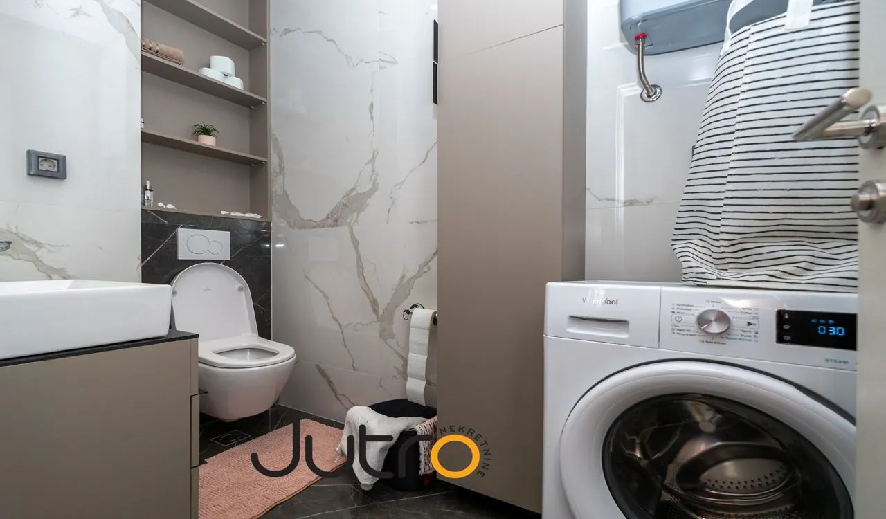 Savremeno opremljeno kupatilo sa WC šoljom, umivaonikom i veš mašinom.