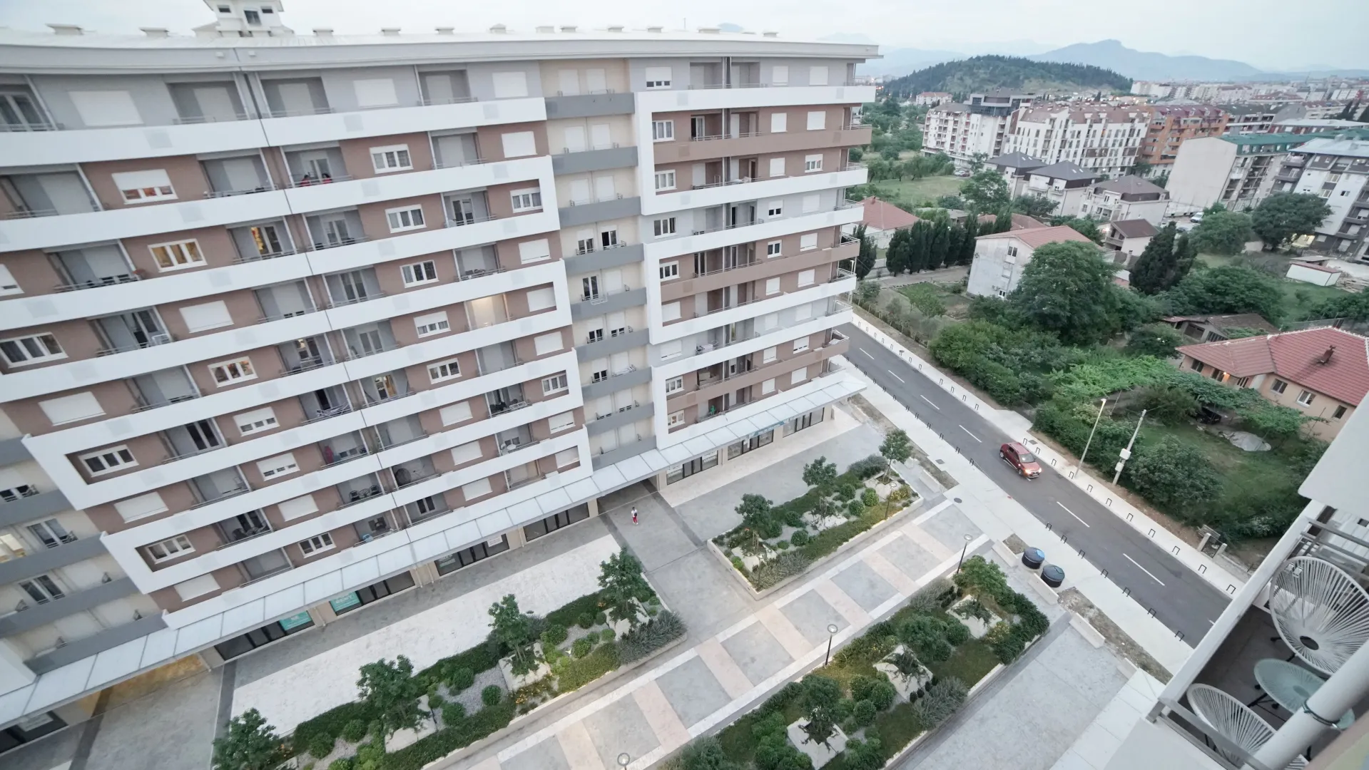 Pogled sa terase na višespratnu stambenu zgradu i uređen plato ispred ulaza.