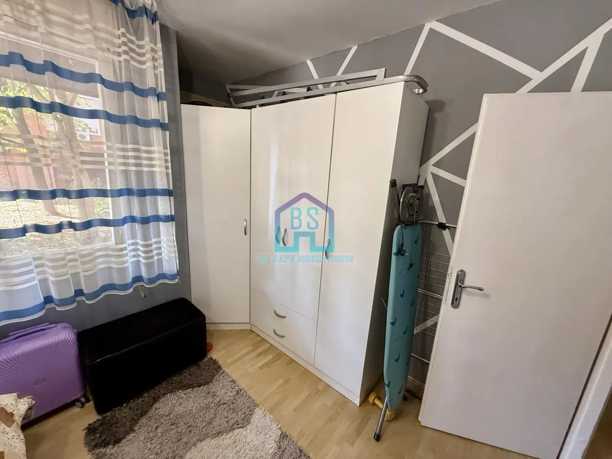Manja spavaća soba sa belim garderoberom, prozorom sa plavim zavesama i laminatnim podom.
