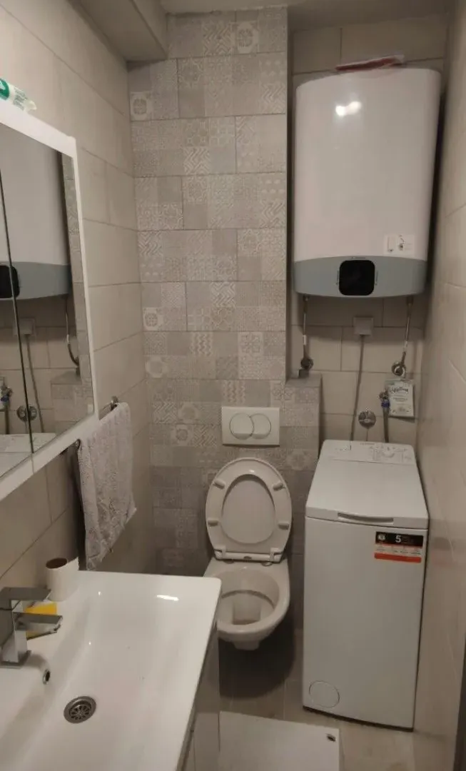 Small bathroom with a sink, toilet, washing machine, and water heater.