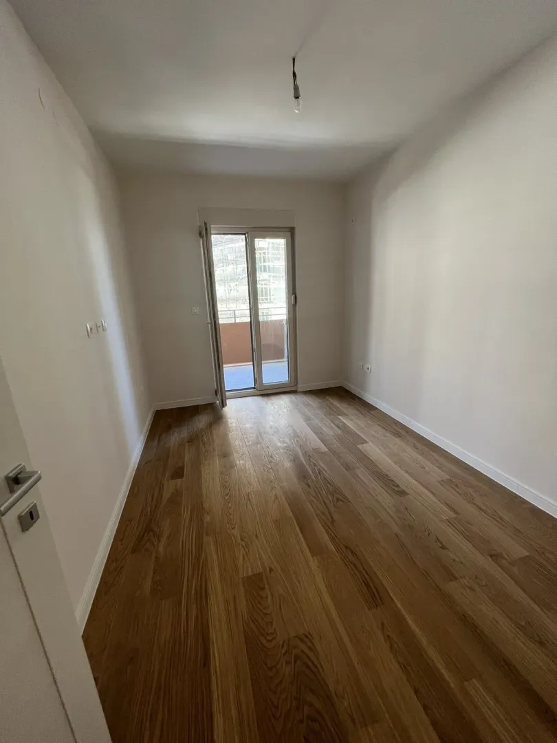 Empty, bright room with wooden flooring and balcony access.