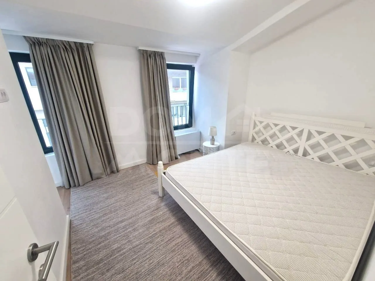 Bright bedroom with a white bed, carpet, and windows with curtains.