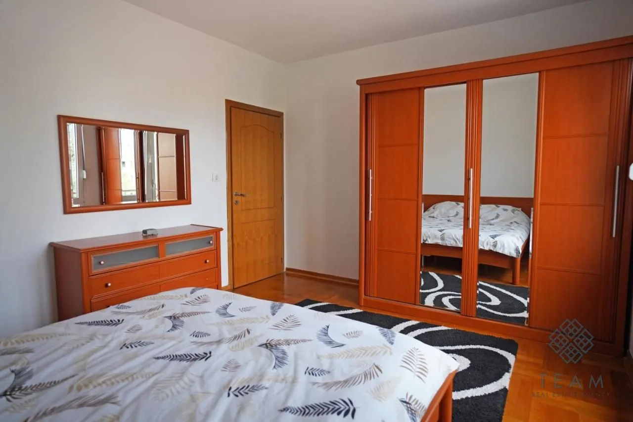Furnished bedroom with a double bed, a large wooden wardrobe, and a dresser with a mirror.