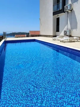 Vanjski bazen sa popločanim platoom i ležaljkama pored zgrade. - image 14