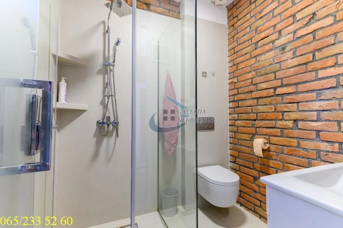 Moderno kupatilo sa tuš kabinom i zidom od cigle.