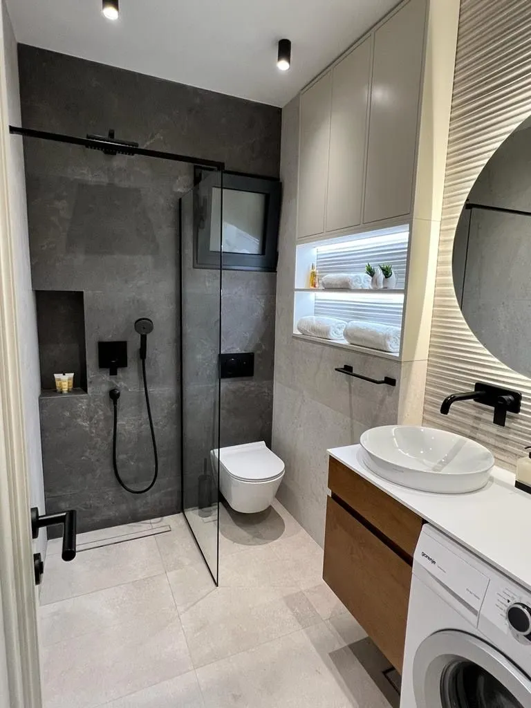 Modern bathroom with a walk-in shower, washbasin, and washing machine.