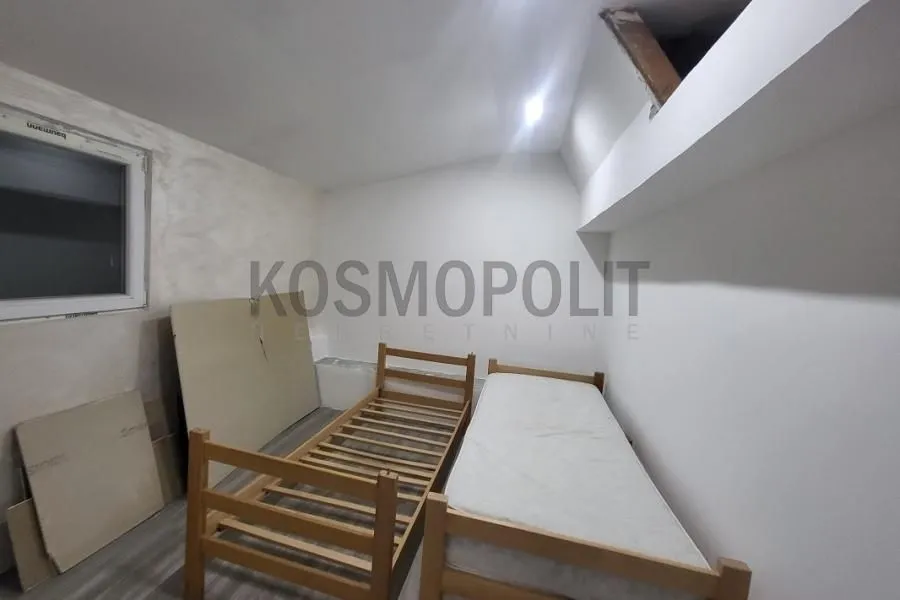 Attic bedroom with two wooden beds and white walls.