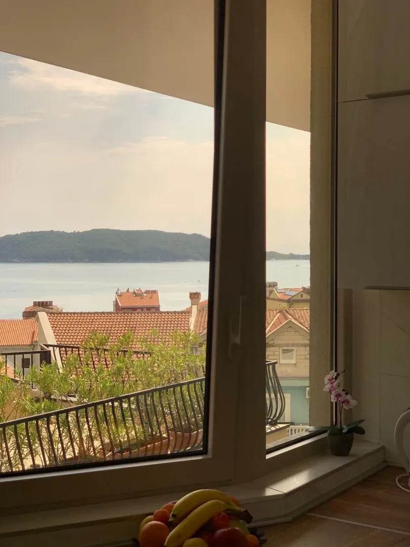 Pogled na more i krovove grada kroz prozor.