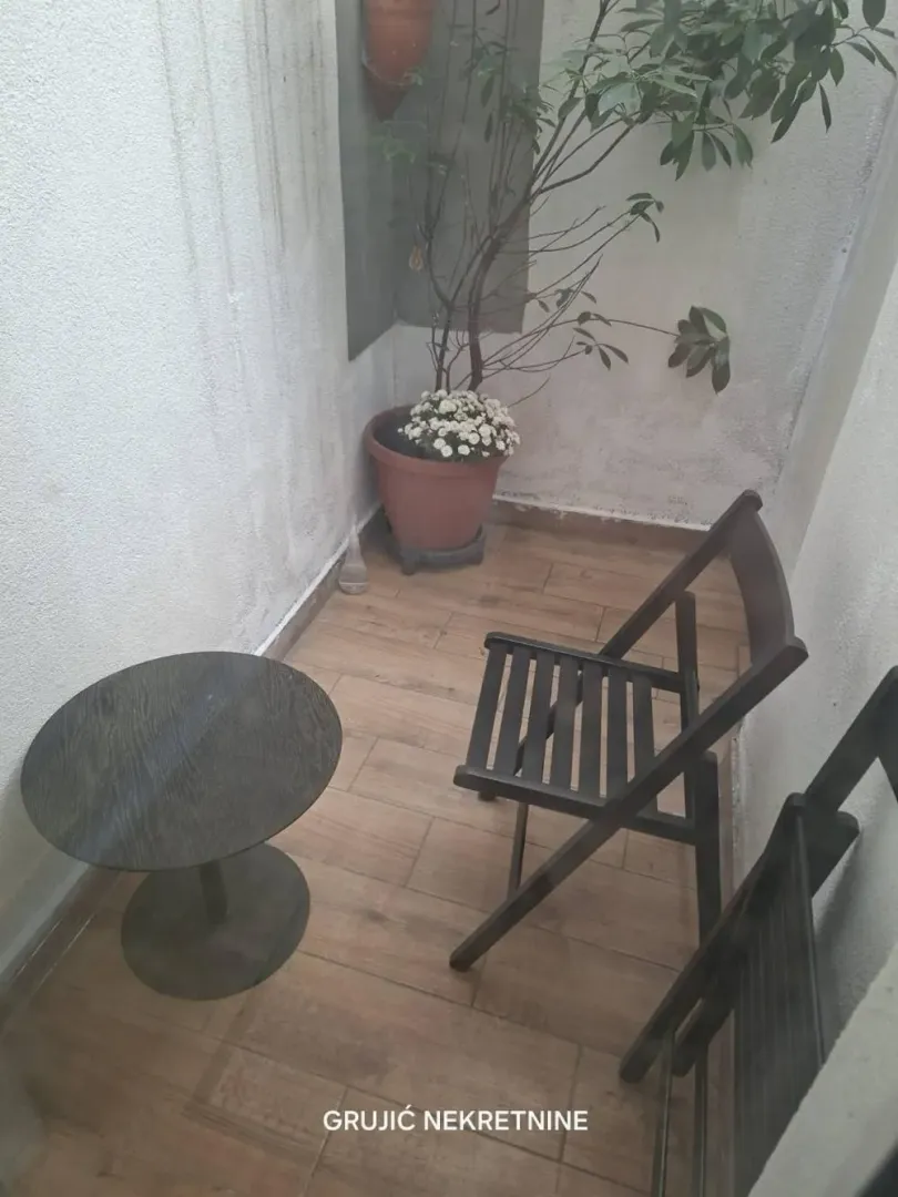Small balcony with wooden flooring, a small table, chairs, and a potted plant.