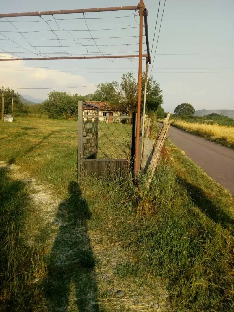 Seosko imanje sa dvorištem, kapijom i pomoćnim objektom pored puta.