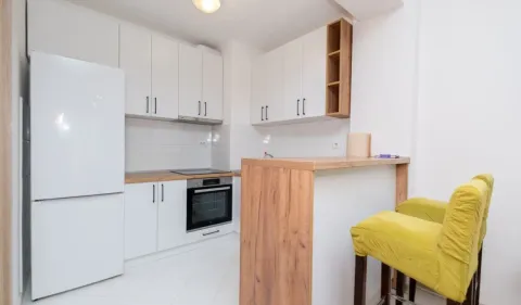 Bijela kuhinja sa drvenim radnim elementima i šankom sa žutim stolicama. - image 4