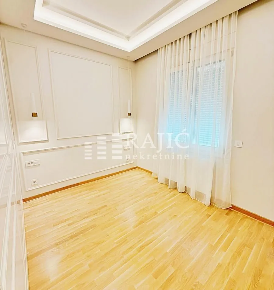 Empty room with wooden flooring, white walls, and curtains on the window.