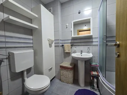 Kompaktno kupatilo sa umivaonikom, WC šoljom i tuš kabinom obloženo sivo-bijelim pločicama. - image 9