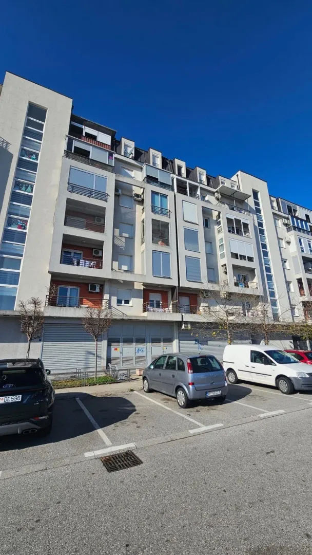 Pogled na spoljašnjost stambene zgrade sa parkingom.