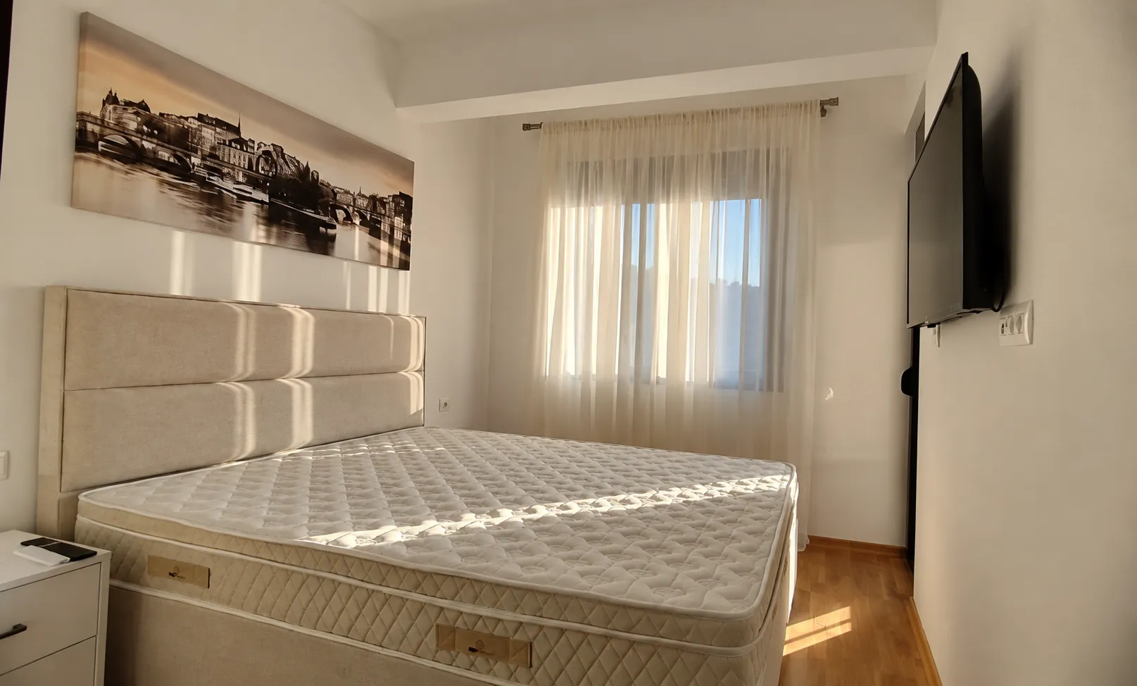 Bedroom with a double bed, wall-mounted TV, and a window with curtains.