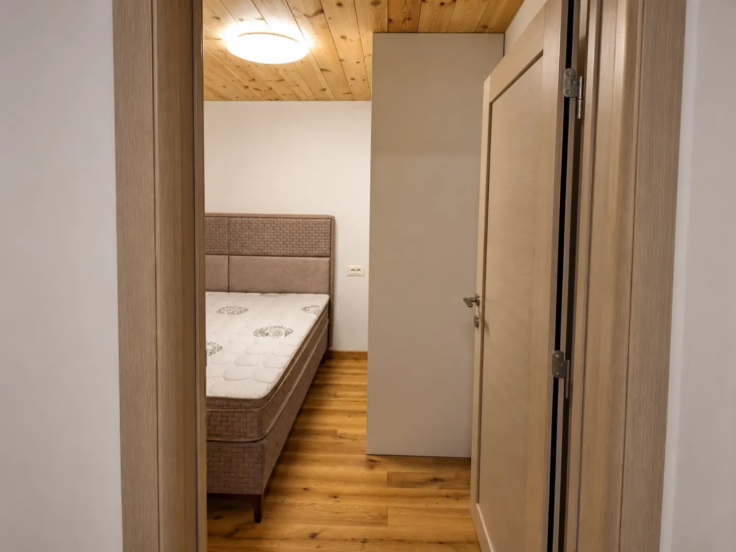Pogled iz hodnika na spavaću sobu sa krevetom i drvenim plafonom.